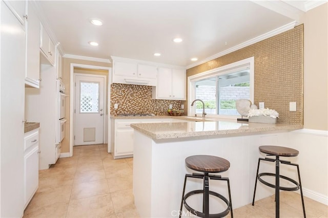 kitchen with a sink, a peninsula, white cabinetry, a breakfast bar, and crown molding
