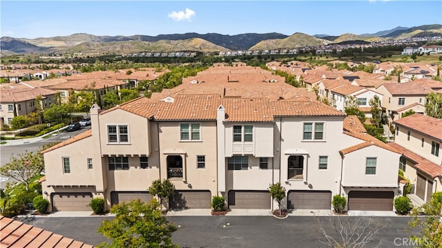 view of front of home featuring an attached garage, stucco siding, a residential view, a mountain view, and driveway