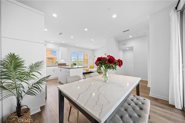 kitchen with a center island, light wood-type flooring, white cabinetry, recessed lighting, and a breakfast bar area