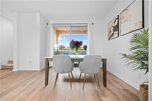 dining area with light wood finished floors, stairs, and baseboards