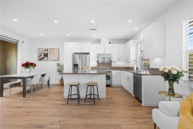 kitchen featuring stainless steel appliances, a kitchen bar, dark countertops, a center island, and recessed lighting