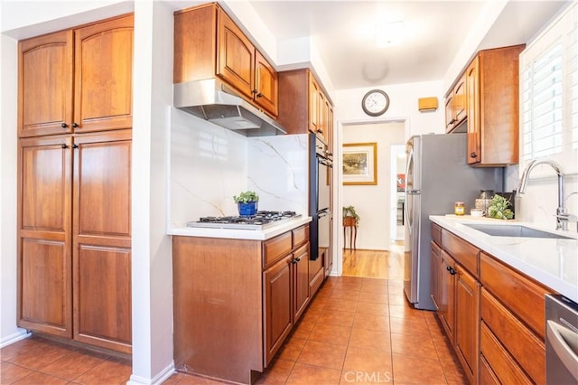 kitchen featuring under cabinet range hood, a sink, stainless steel appliances, light countertops, and tile patterned floors