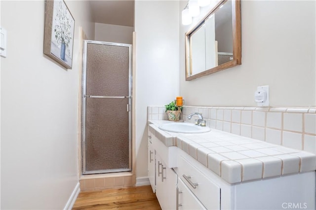 bathroom with a stall shower, wood finished floors, vanity, baseboards, and decorative backsplash