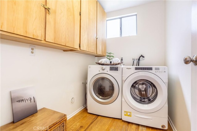 clothes washing area with washing machine and dryer, light wood-style flooring, cabinet space, and baseboards