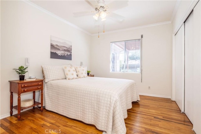 bedroom featuring light wood finished floors, crown molding, a closet, baseboards, and a ceiling fan