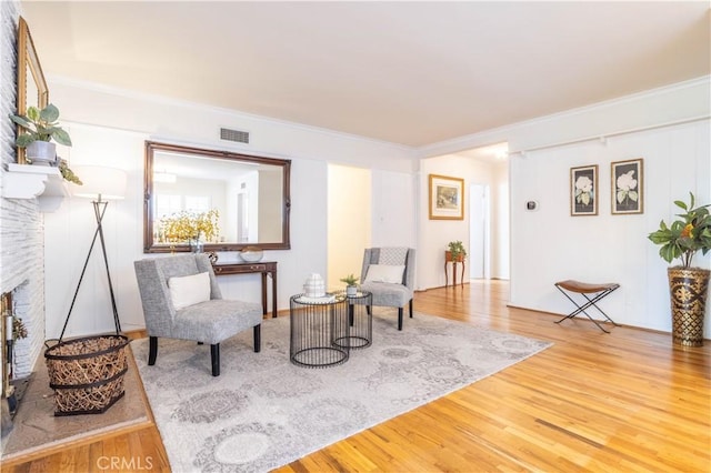 sitting room featuring wood finished floors, crown molding, and a stone fireplace