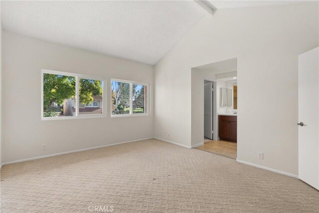 unfurnished bedroom with light carpet, baseboards, beam ceiling, high vaulted ceiling, and ensuite bathroom