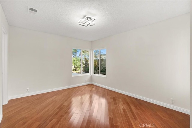 spare room with wood finished floors, baseboards, and a textured ceiling