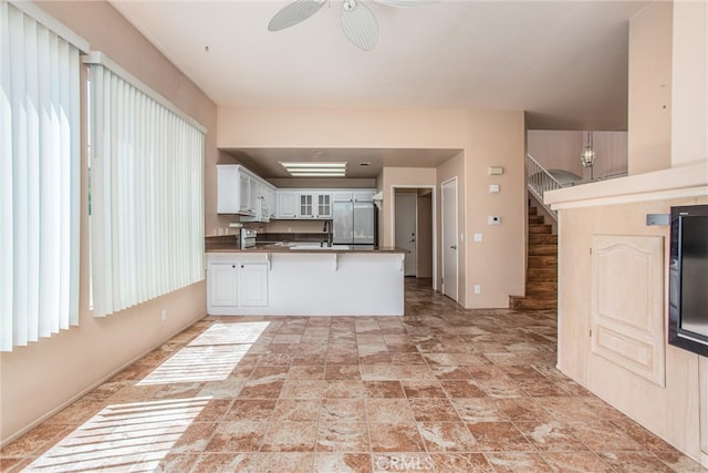 588 Twin Hills Dr, Banning, CA 92220 - kitchen with a peninsula, glass insert cabinets, light stone finish flooring, white cabinetry, and ceiling fan