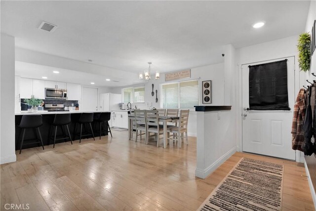 21046 Lone Eagle Rd, Apple Valley, CA 92308 - kitchen featuring appliances with stainless steel finishes, a chandelier, a kitchen bar, white cabinets, and light wood-style flooring