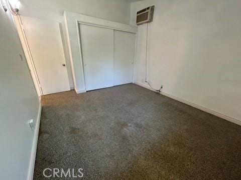 8960 Indiana Ave, Riverside, CA 92503 - unfurnished bedroom with a wall unit AC, dark carpet, a closet, and baseboards