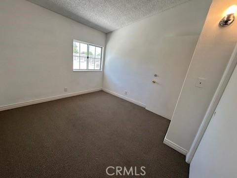 8960 Indiana Ave, Riverside, CA 92503 - unfurnished room with a textured ceiling, dark colored carpet, and baseboards