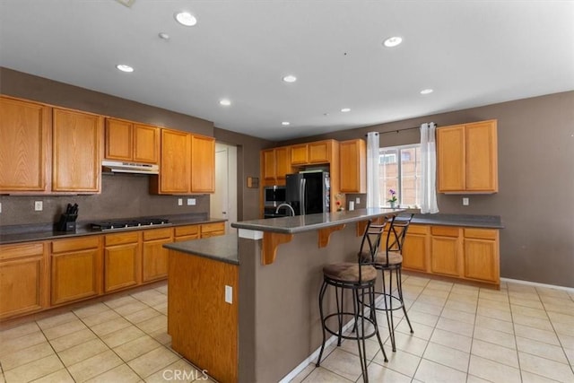 16549 Gala Ave, Fontana, CA 92337 - kitchen featuring under cabinet range hood, freestanding refrigerator, light tile patterned floors, a kitchen breakfast bar, and an island with sink