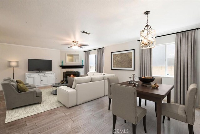 5354 Wrangler Dr, Fontana, CA 92336 - living area featuring light wood-style floors, a chandelier, a ceiling fan, a warm lit fireplace, and crown molding