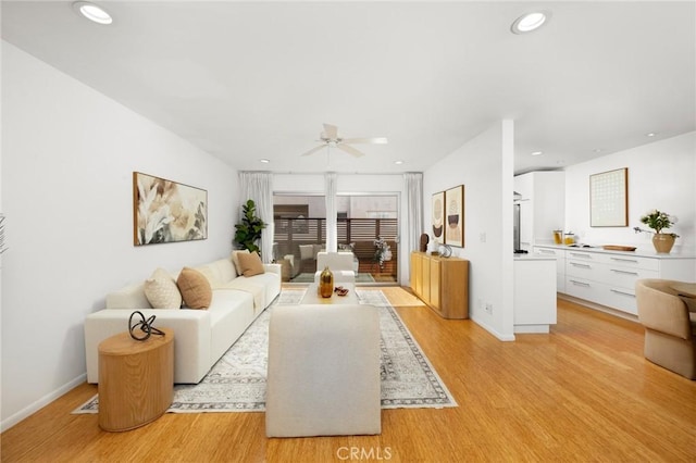 living room featuring light wood-type flooring, a ceiling fan, recessed lighting, and baseboards