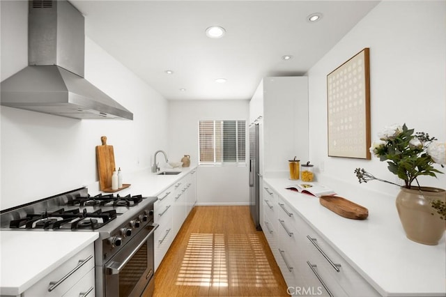 kitchen featuring appliances with stainless steel finishes, wall chimney exhaust hood, light wood-style flooring, a sink, and white cabinets