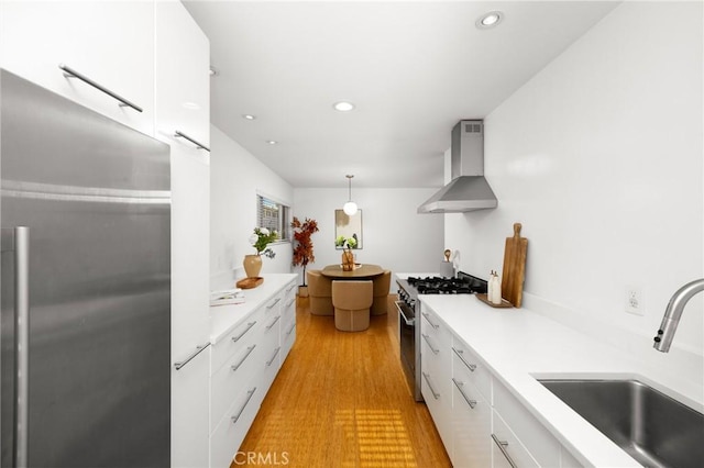 kitchen with wall chimney range hood, appliances with stainless steel finishes, a sink, modern cabinets, and light countertops