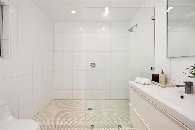 bathroom featuring tiled shower, toilet, tile walls, vanity, and tile patterned flooring