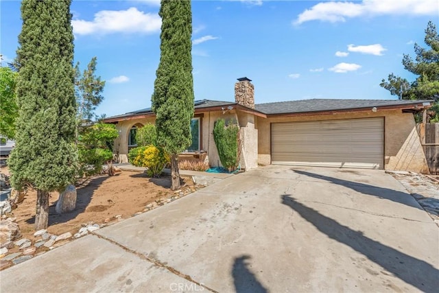 16230 Rodeo St, Hesperia, CA 92345 - view of front facade with concrete driveway, solar panels, stucco siding, a garage, and a chimney