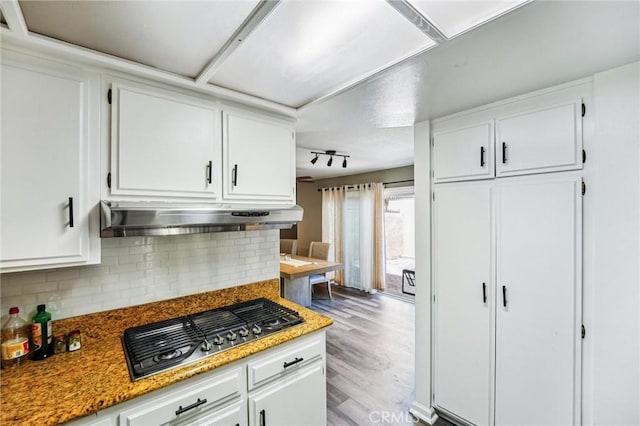kitchen featuring stainless steel gas stovetop, under cabinet range hood, white cabinets, decorative backsplash, and wood finished floors