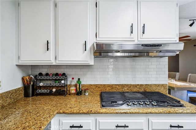 kitchen with under cabinet range hood, stainless steel gas stovetop, white cabinetry, decorative backsplash, and light stone countertops