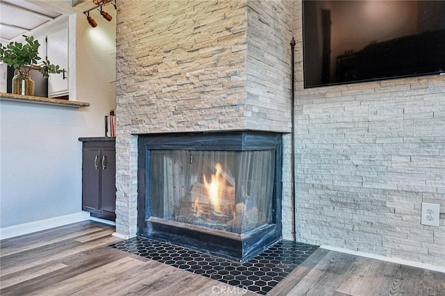 detailed view of wood finished floors, baseboards, and a stone fireplace