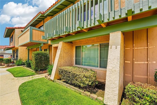 view of side of home with a balcony, stucco siding, and a tile roof