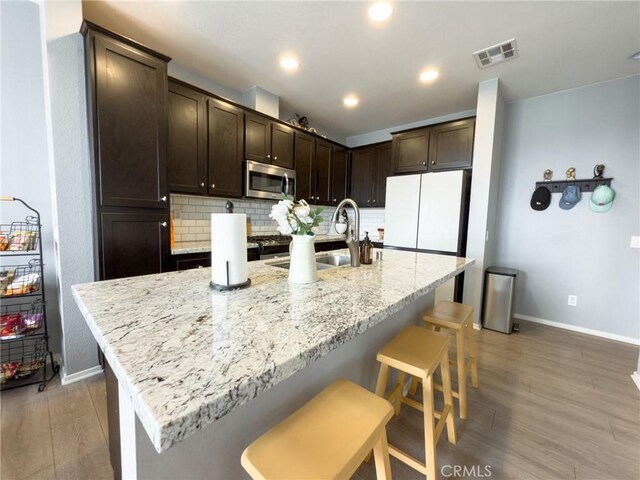 5485 San Roberto, San Diego, CA 92154 - kitchen with stainless steel microwave, baseboards, dark brown cabinets, light wood-style flooring, and backsplash