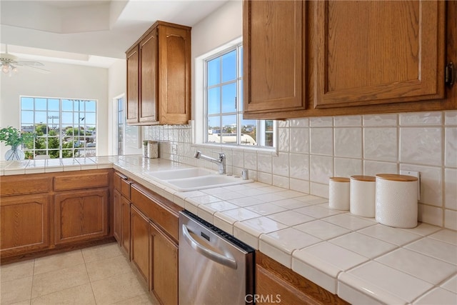 kitchen featuring stainless steel dishwasher, a sink, brown cabinets, decorative backsplash, and healthy amount of natural light