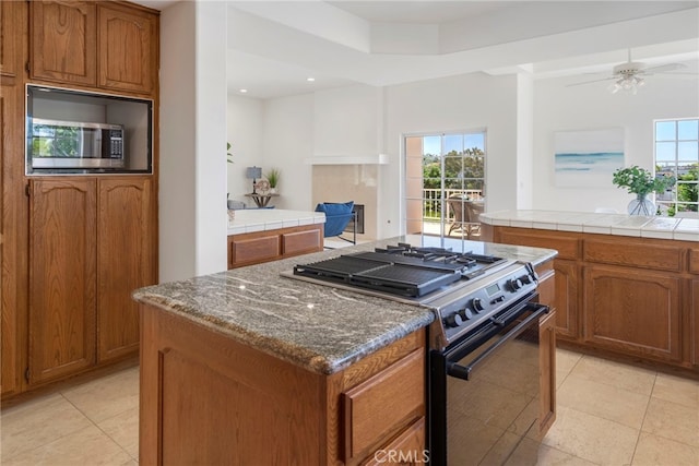 kitchen featuring gas range oven, stainless steel microwave, brown cabinets, light tile patterned flooring, and recessed lighting