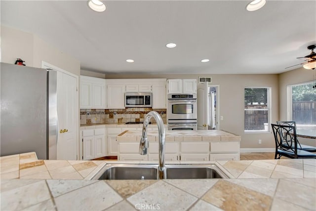 24062 Fuschia Ct, Murrieta, CA 92562 - kitchen featuring appliances with stainless steel finishes, a sink, tile countertops, tasteful backsplash, and white cabinetry