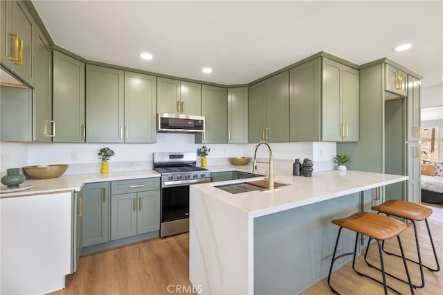 21408 Apollo Way, Desert Hot Springs, CA 92241 - kitchen with stainless steel appliances, green cabinets, a sink, light wood-style floors, and a breakfast bar