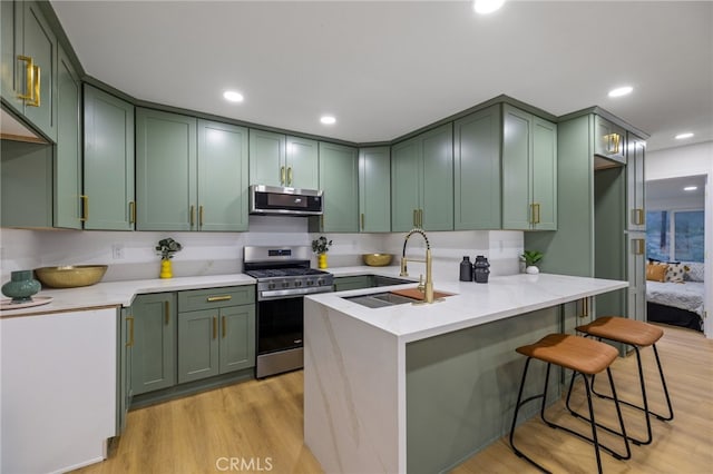 21408 Apollo Way, Desert Hot Springs, CA 92241 - kitchen featuring appliances with stainless steel finishes, a sink, green cabinetry, light wood-style floors, and a kitchen bar