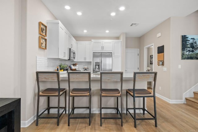 1211 Sunrise Vw Unit 104, San Marcos, CA 92078 - kitchen featuring appliances with stainless steel finishes, a peninsula, white cabinets, a breakfast bar area, and light wood-style flooring