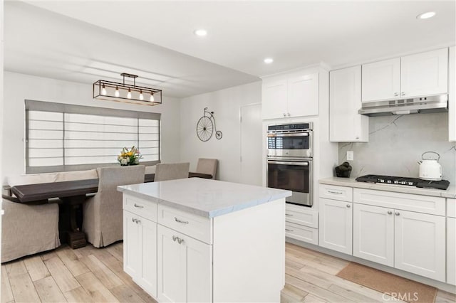 kitchen with under cabinet range hood, gas stovetop, light wood-style floors, double oven, and recessed lighting