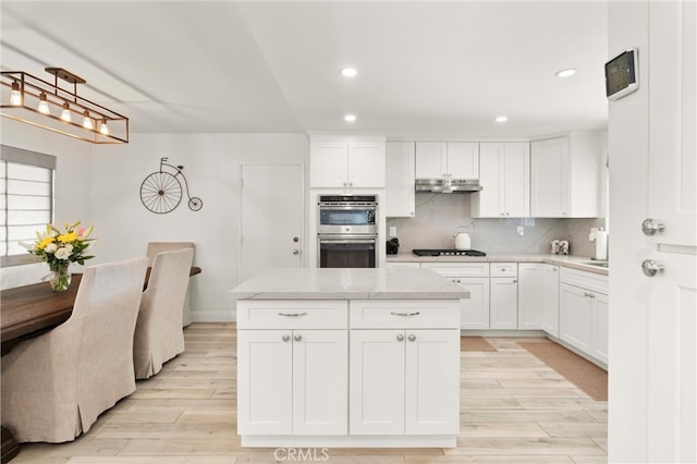 kitchen with stainless steel double oven, light wood-type flooring, under cabinet range hood, recessed lighting, and gas cooktop