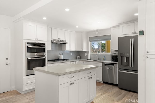 kitchen featuring stainless steel appliances, a sink, light wood-type flooring, decorative backsplash, and under cabinet range hood