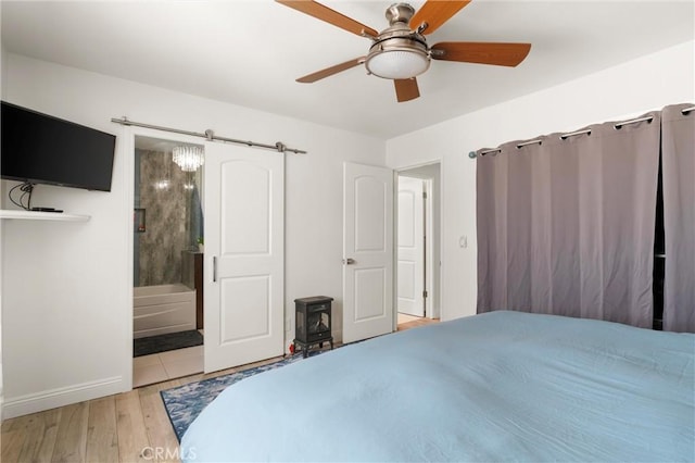 bedroom featuring wood finished floors, a wood stove, baseboards, connected bathroom, and ceiling fan