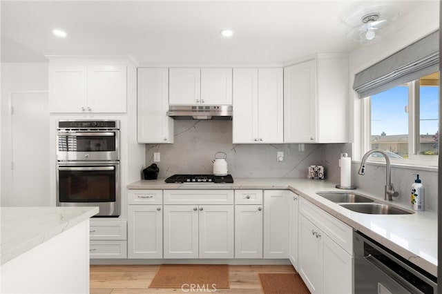 kitchen with dishwasher, a sink, under cabinet range hood, black gas cooktop, and stainless steel double oven