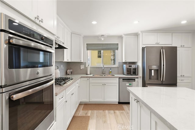 kitchen featuring appliances with stainless steel finishes, a sink, white cabinets, light wood-type flooring, and decorative backsplash