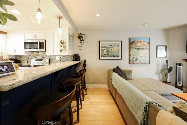 290 Victoria St Unit 19, Costa Mesa, CA 92627 - kitchen featuring stainless steel microwave, range with gas stovetop, backsplash, a kitchen bar, and white cabinetry