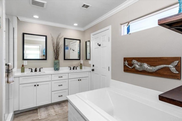 bathroom with ornamental molding, a bath, double vanity, recessed lighting, and wood finished floors