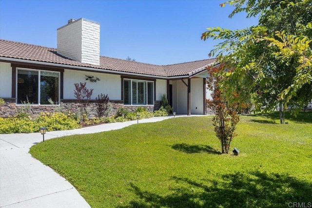 view of front of property with stone siding, a chimney, a front lawn, and a tiled roof
