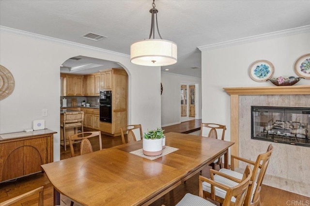 dining room featuring arched walkways, crown molding, wood finished floors, and a tiled fireplace