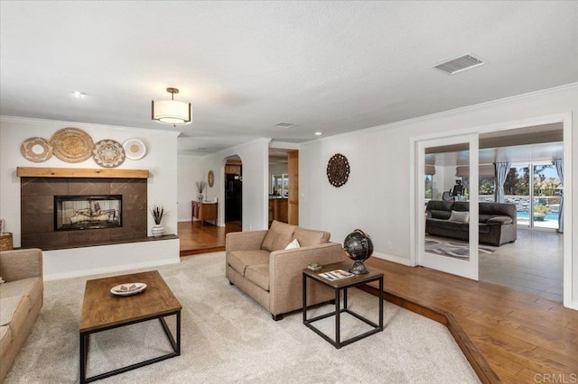 living room featuring arched walkways, light wood-style floors, ornamental molding, baseboards, and a fireplace