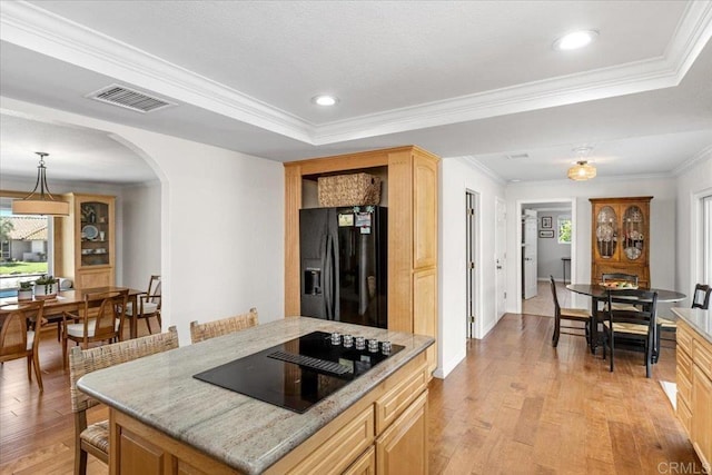 kitchen featuring black appliances, arched walkways, light wood finished floors, a raised ceiling, and light brown cabinets