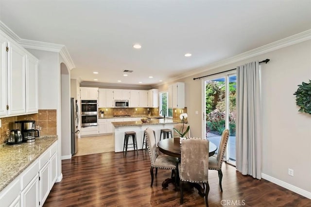 dining space with arched walkways, crown molding, dark wood-style flooring, recessed lighting, and baseboards