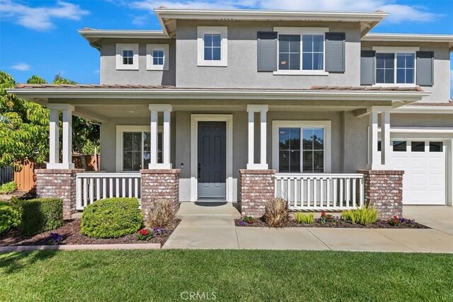 prairie-style home featuring a porch, stucco siding, an attached garage, and brick siding