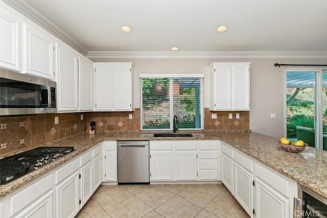 kitchen with appliances with stainless steel finishes, a sink, light tile patterned flooring, white cabinets, and crown molding