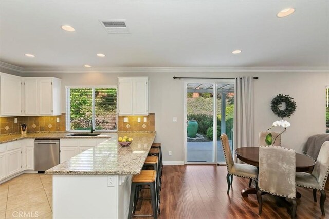 kitchen featuring stainless steel dishwasher, a sink, healthy amount of natural light, light stone counters, and recessed lighting